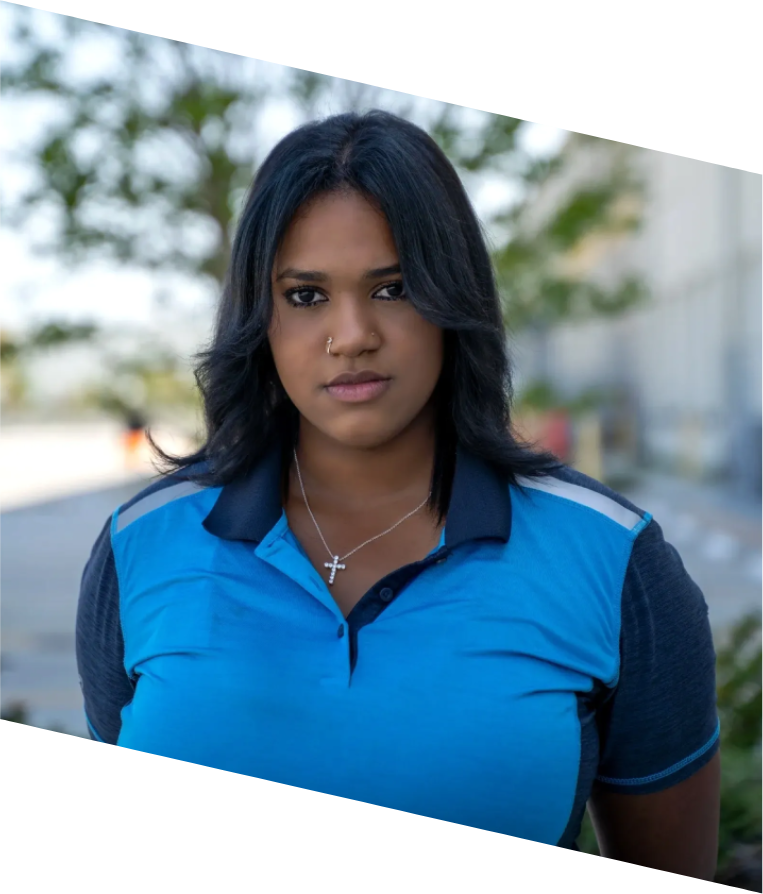 A woman in blue shirt and necklace standing on street.